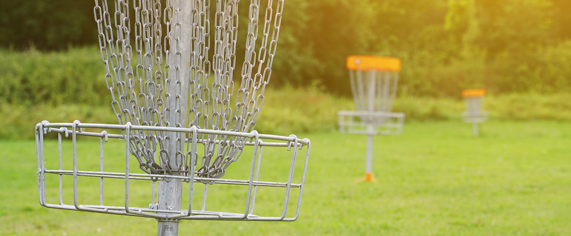 A disc golf basket with chains hanging from the pole stands in a grassy field with additional baskets visible in the background.